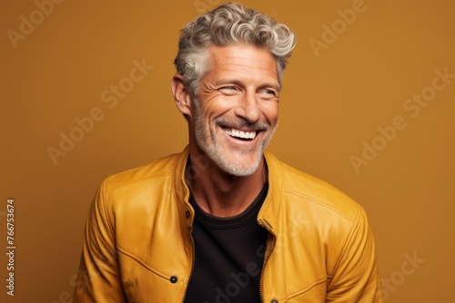 Handsome middle-aged man laughing and looking at camera while standing against orange background © Inigo
