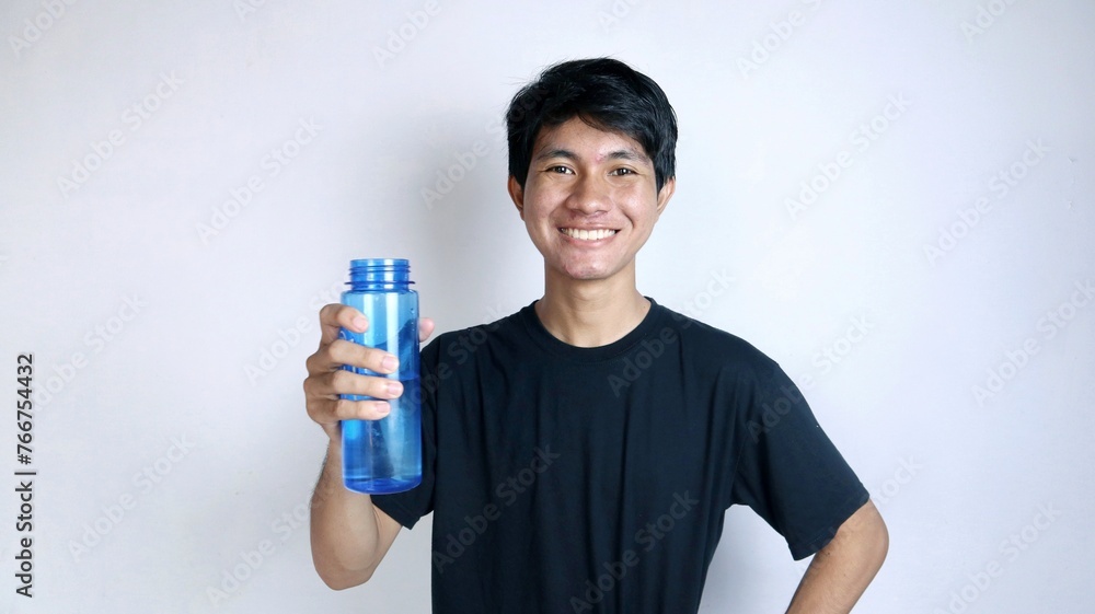Handsome young Asian man smiling gesturingly holding a drinking water bottle Handsome young Asian man smiling gesturingly holding a drinking water bottle