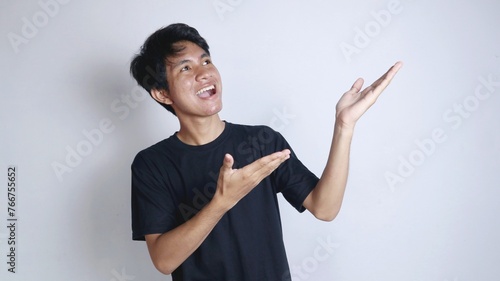 Young Asian man smiling gesturing with open palm pointing to the left side photo