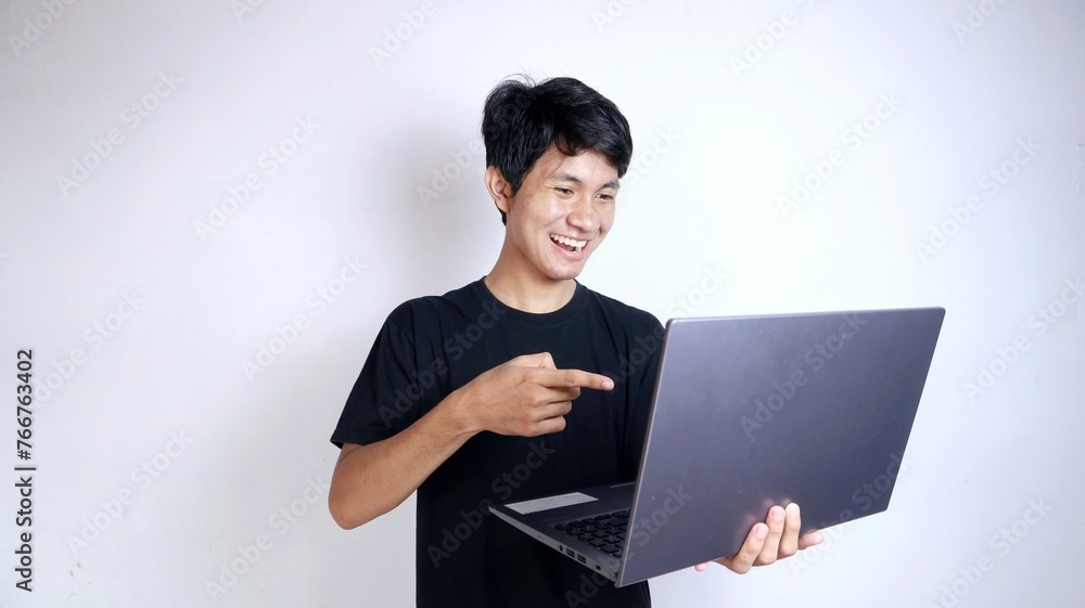 Excited young Asian man with gestures holding a laptop while pointing at the laptop Excited young Asian man with gestures holding a laptop while pointing at the laptop