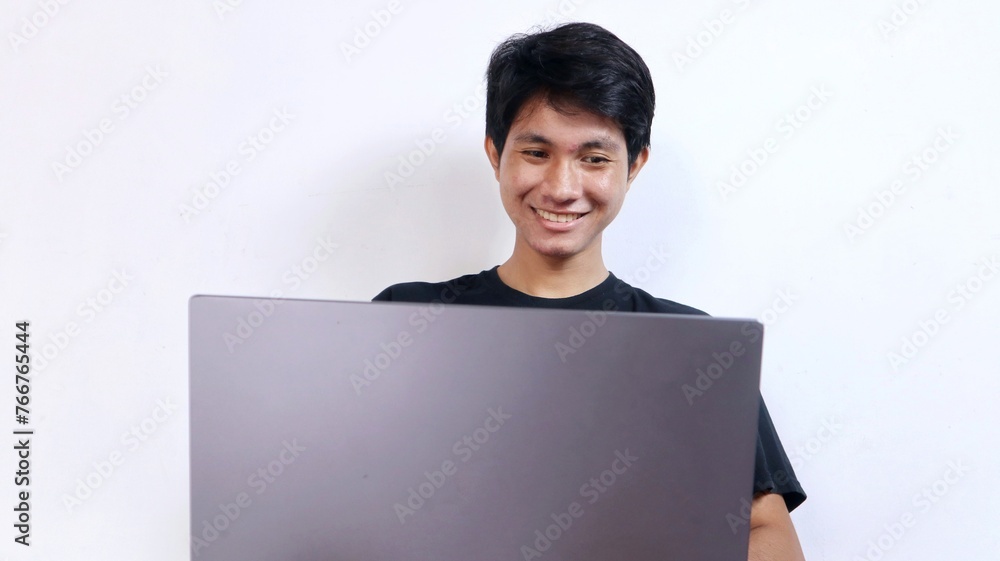 Young happy Asian man with gesture sitting on a chair using a laptop Young happy Asian man with gesture sitting on a chair using a laptop