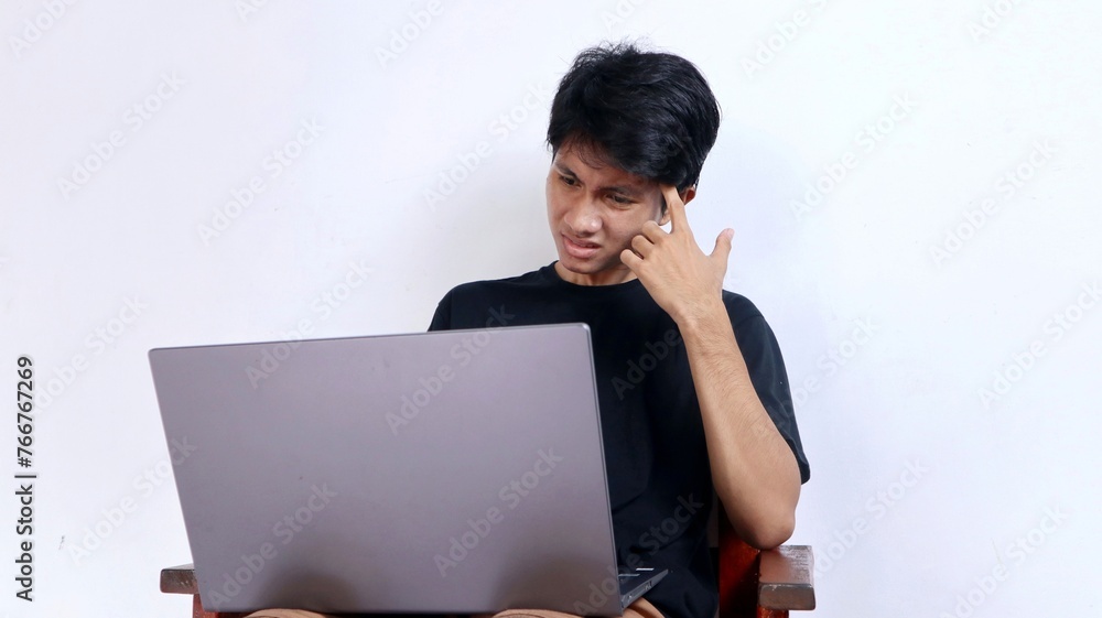 Serious young Asian man sitting doing something in front of a laptop Serious young Asian man sitting doing something in front of a laptop