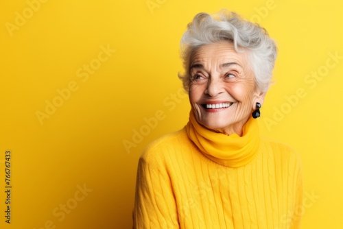 Portrait of a smiling senior woman in yellow sweater on yellow background