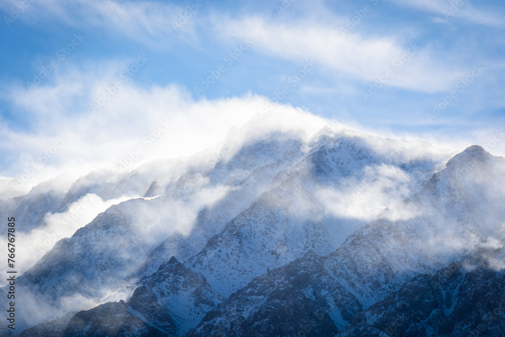 A closeup view of a mountain peak covered in snow as the wind swirls clouds around it. Aspen Springs, California - Highway 395