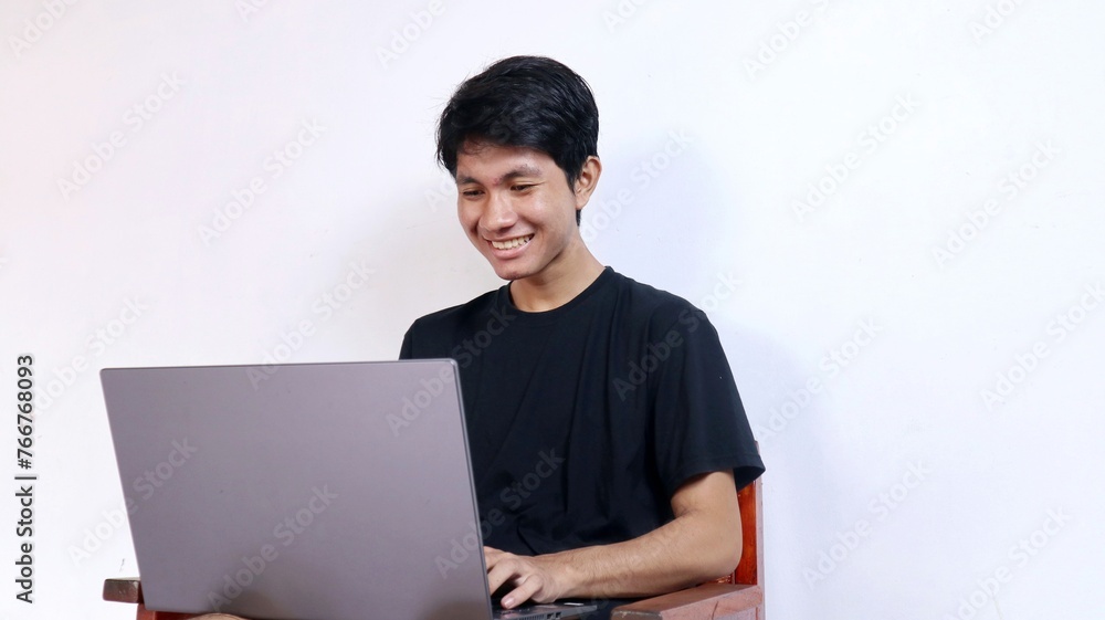 Young happy Asian man with gesture sitting on a chair using a laptop Young happy Asian man with gesture sitting on a chair using a laptop