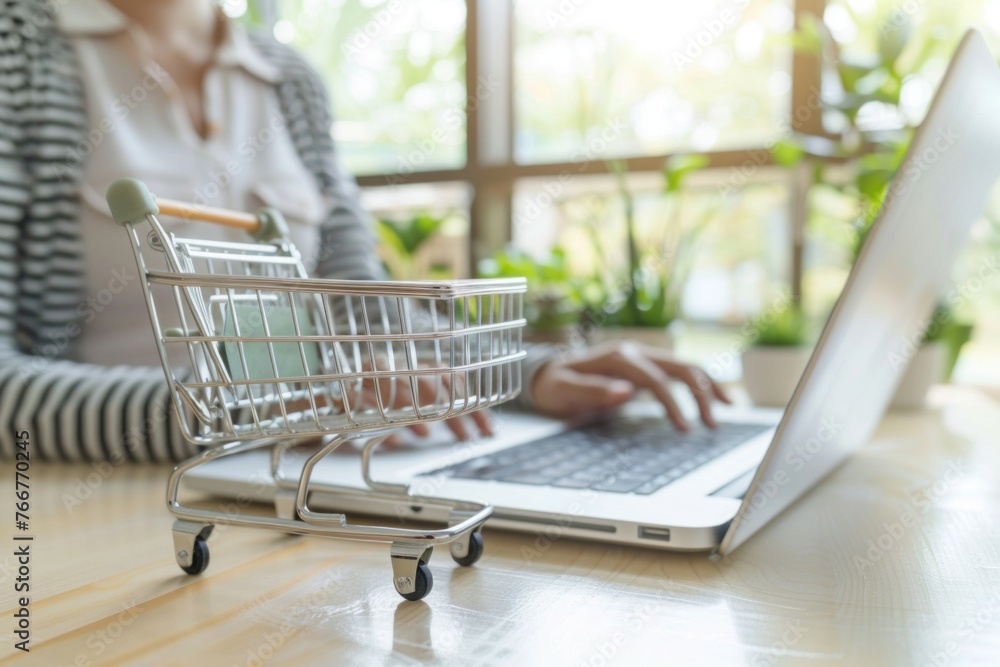 card box small in shopping cart with businesswomen using laptop on a desk, e-commerce, and delivery online business concept. card box small in shopping cart with businesswomen using laptop on a desk, e-commerce, and delivery online business concept.