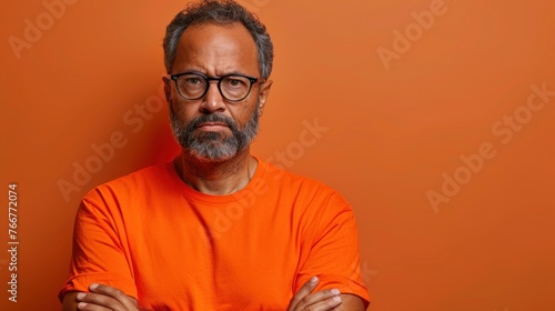 A man wearing an orange shirt stands with his arms crossed