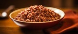 A bowl of brown rice, a staple food and superfood, is on a wooden table next to a spoon. This ingredient can be used in various recipes from different cuisines