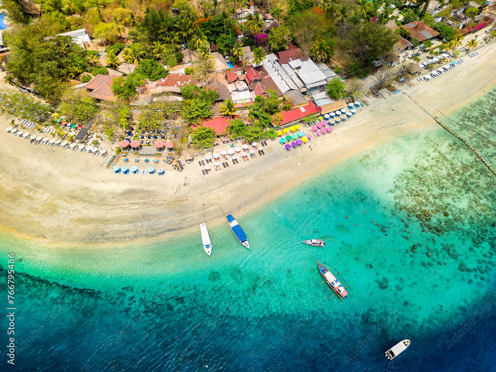 Aerial view of a sandy tropical beach and small resorts next to a warm ocean and coral reef (Gili Islands)