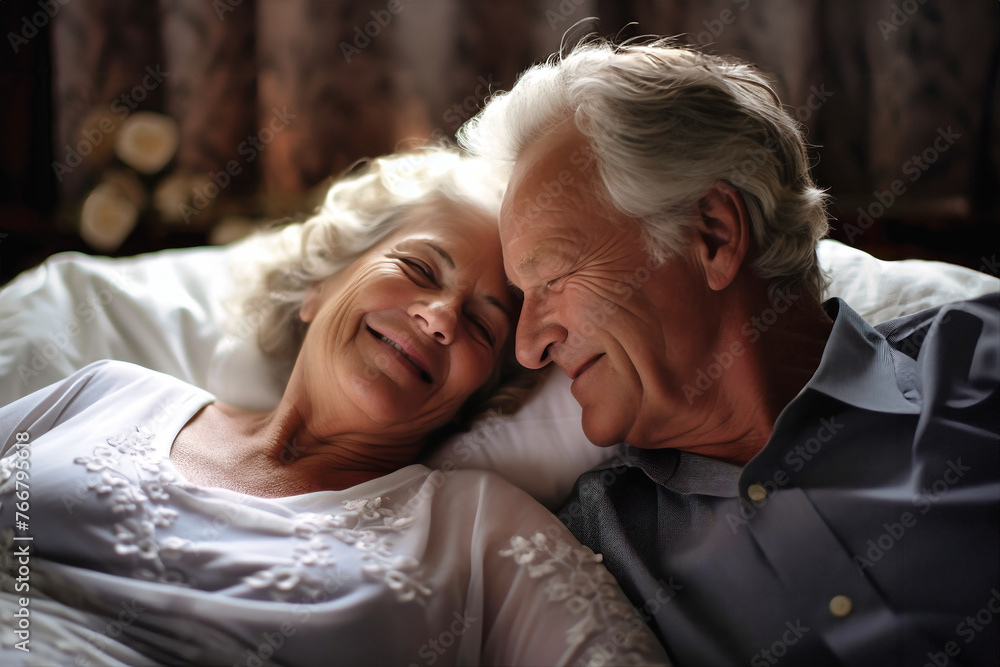 An older man and woman embrace tenderly under a warm blanket on a bed, demonstrating love and intimacy