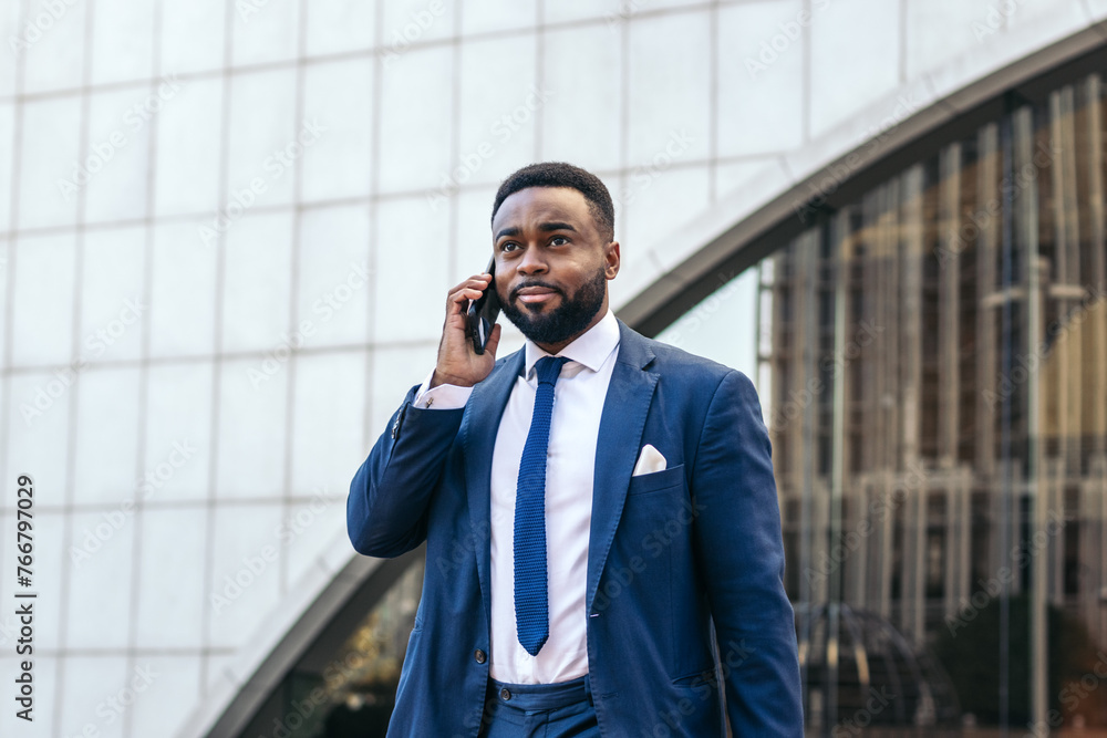 Business black man in suit talking on the phone while leaving the office Business black man in suit talking on the phone while leaving the office