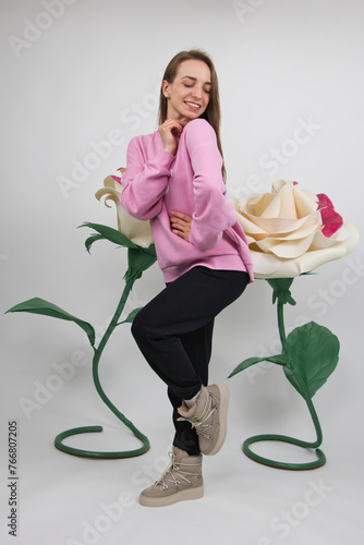 A girl in sportswear poses with a smile against the background of large artificial white roses. studio shot