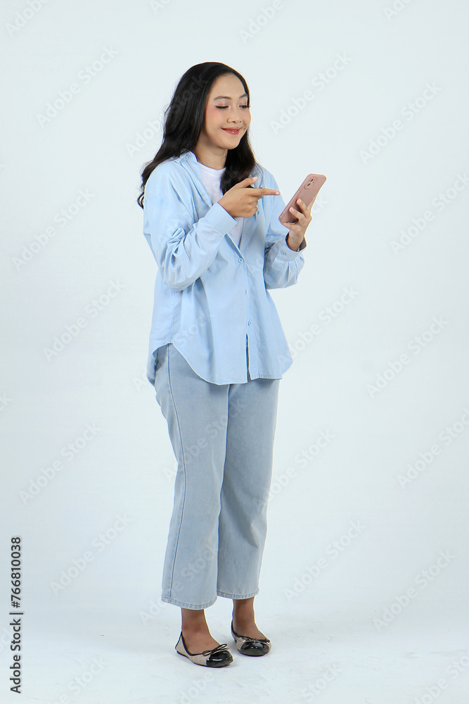 full lenght shoot of happy asian indonesian woman holding smartphone and with pointing finger gesture on isolated background full lenght shoot of happy asian indonesian woman holding smartphone and with pointing finger gesture on isolated background