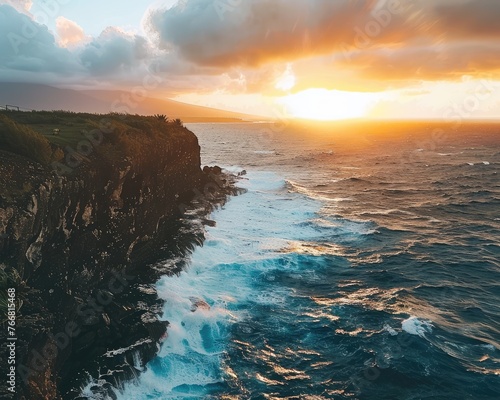 A dramatic cliffside view of the ocean at sunrise with waves crashing below