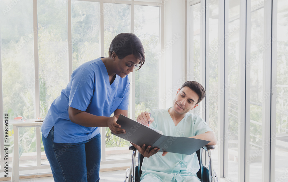 Fototapeta premium Portrait patient caucasian man sit wheelchair with woman nurse carer physical therapist African-American two people talk sign important documents advice feel relax smile happy in hospital room service