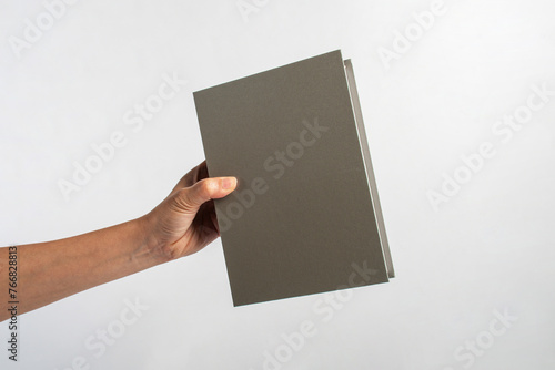 Blank grey book cover in hand on white background. © apinya