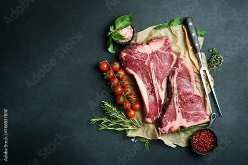 Dry-aged Raw T-bone or porterhouse beef steak with herbs and salt. On a black stone background. Barbecue.