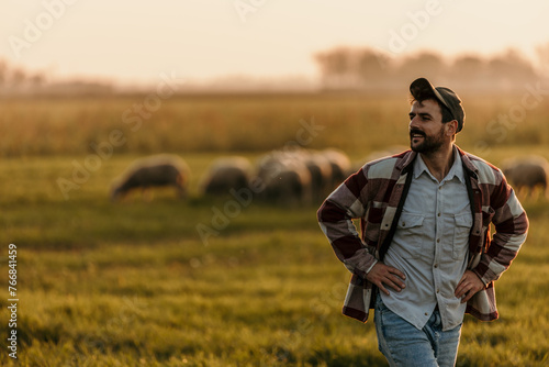 Farmer takes a moment to appreciate the simple joys of rural life amidst his field at sunset, sheep meandering in the distance © La Famiglia