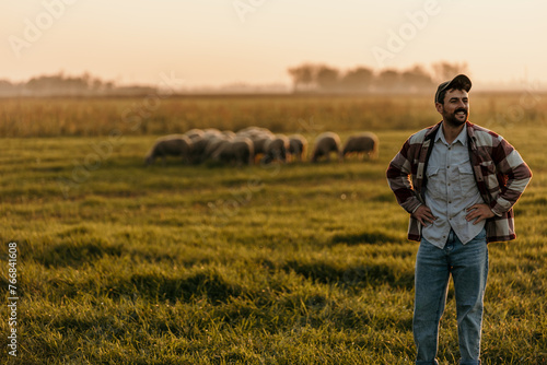 Farmer admires the golden hues of the setting sun over his pastoral field, with sheep dotting the landscape