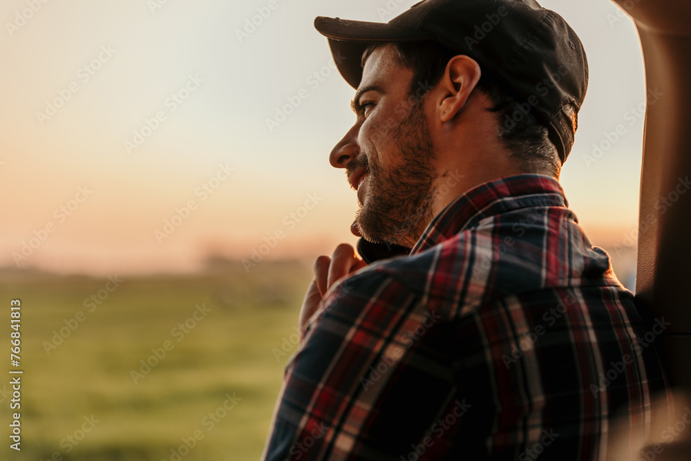 A young man seated comfortably in the back of a truck, talking on his phone as the sun sets in the background