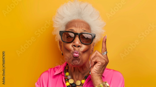 A spirited elderly woman with sunglasses pointing with panache against an orange backdrop.