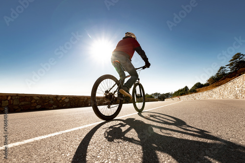 Silhouette of man athlete is riding on mtb bike at mountain road against sun and sky