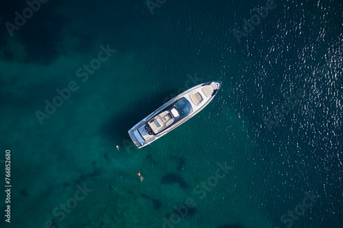 Modern yacht on clear blue water from above. People swim around the yacht, top view. Expensive yacht on blue water aerial view.