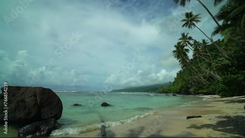 Taveuni Garden Island Tavern Falls beach walk coral sand tropical peaceful waves crashing shoreline palm coconut trees sunny blue sky cloudy boulder clear water slow pan to the right photo