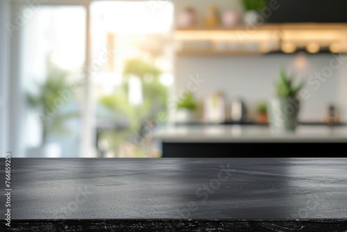 The sleek black surface of a modern kitchen table stands out against the blurred background of a bright and airy kitchen space with green plants