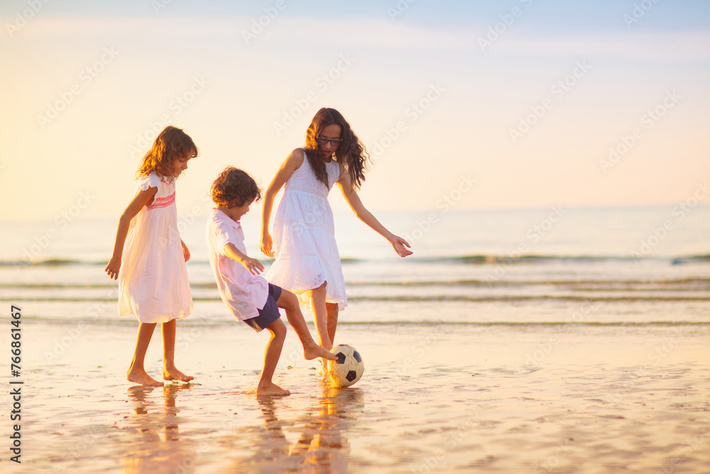 Kids play football on tropical beach at sunset