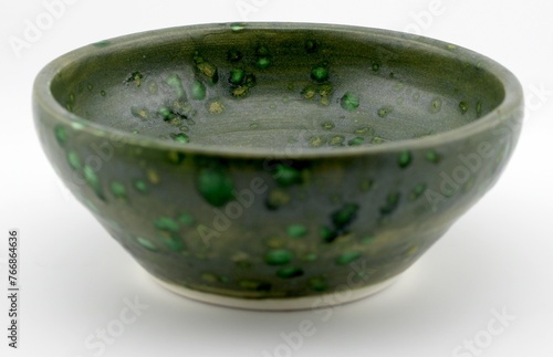 A green and white ceramic bowl sits atop a wooden table. The bowl is empty and shows a simple, elegant design.