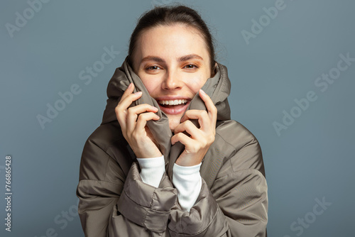 Young cheerful attractive woman wearing a grey coat during autumn and winter, isolated on grey studio background