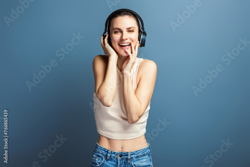 Young cheerful woman enjoying music with headphone, wearing casual top, isolated on grey studio background