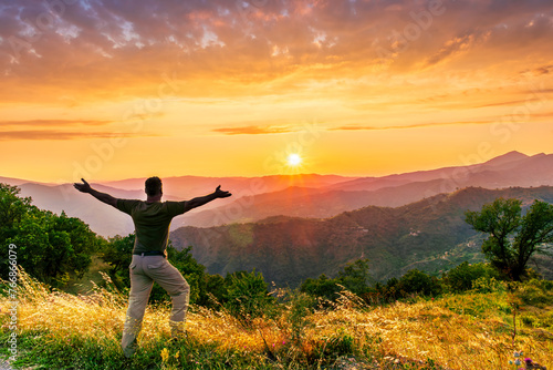 rejoicing man with beautiful scenic mountain sunset landscape on background. happy man watching amazing evening sunset