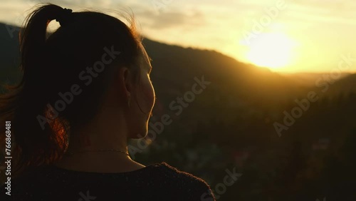 Young woman enjoying sunset in mountains alone. Female hiker portrait looking at scenic landscape of valley at foot of the mountains, rear view