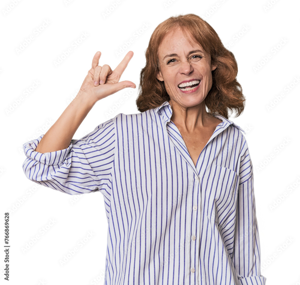 Redhead mid-aged Caucasian woman in studio showing a horns gesture as a revolution concept. Redhead mid-aged Caucasian woman in studio showing a horns gesture as a revolution concept.