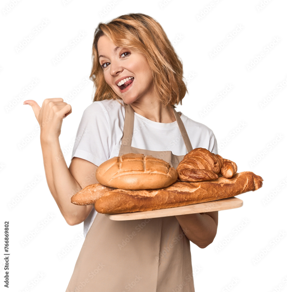 Middle-aged Caucasian woman baker with bread tray points with thumb finger away, laughing and carefree. Middle-aged Caucasian woman baker with bread tray points with thumb finger away, laughing and carefree.