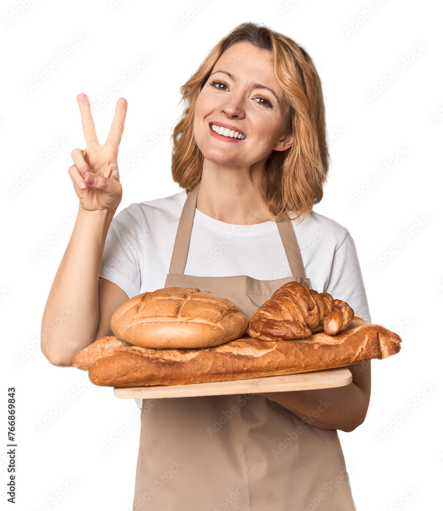 Middle-aged Caucasian woman baker with bread tray showing number two with fingers. Middle-aged Caucasian woman baker with bread tray showing number two with fingers.