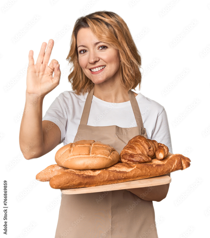 Middle-aged Caucasian woman baker with bread tray cheerful and confident showing ok gesture. Middle-aged Caucasian woman baker with bread tray cheerful and confident showing ok gesture.