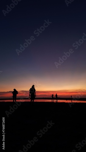 People silhouette are experiencing pure joy as they gather on the beach, delighting in the mesmerizing sunset.