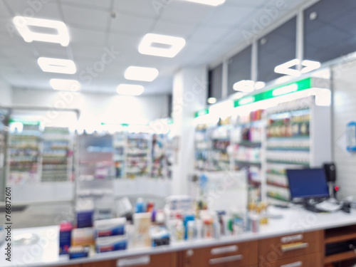 Defocused view inside of pharmacy with the seller counter, computer and cash register against stocked shelves with medicines. Healthcare and cosmetics industry blurred background