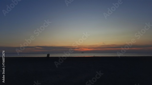 People silhouette are experiencing pure joy as they gather on the beach, delighting in the mesmerizing sunset.