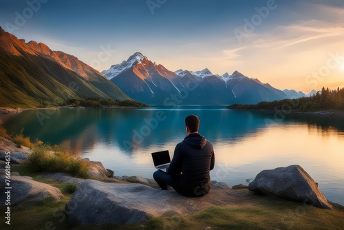 A man is learning something sitting on a rock beside a lake with mountains and sunset a pleasant view