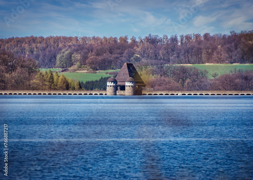 Diese Aufnahme zeigt die imposante Staumauer des Möhnesees, eingebettet in die natürliche Schönheit ihrer Umgebung. Im Hintergrund erheben sich sanfte Berge mit Bäumen. photo