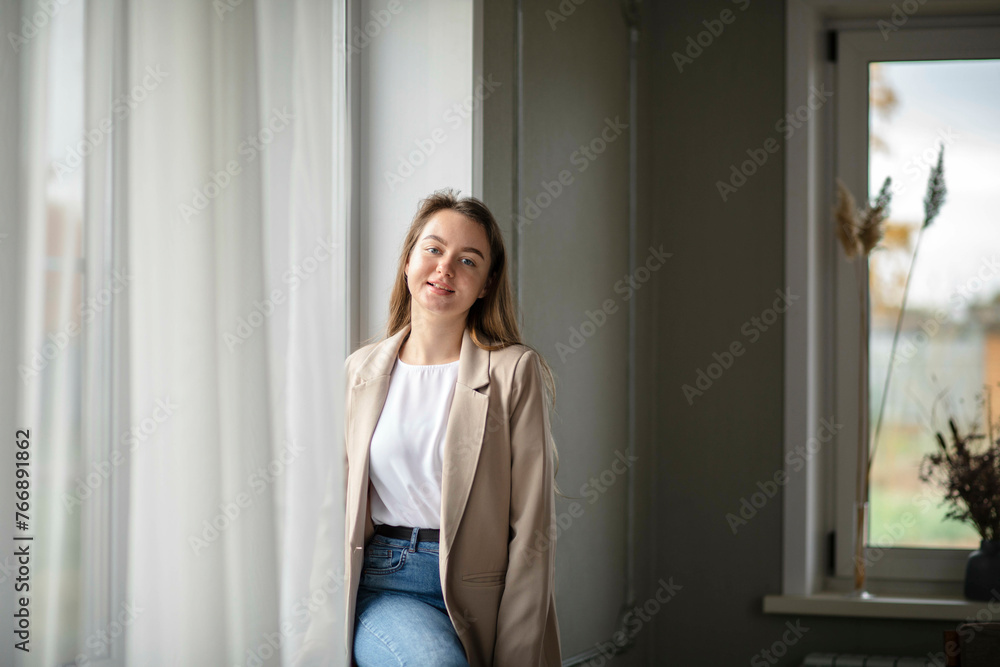 A smiling businesswoman. A small business entrepreneur sitting on the windowsill in hall of her office.