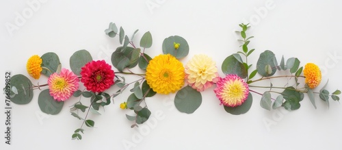 Round yellow and pink flowers incorporated into a floral arrangement with eucalyptus branches on a white backdrop. Presented as a flat lay with a top-down view and room for text.