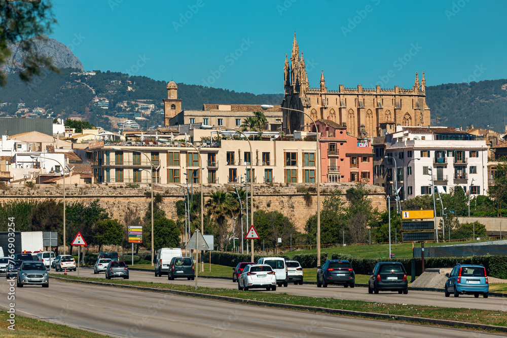 Cars on the urban road as residential buildings and famous cathedral on background in Palma de Mallorca, Soain.