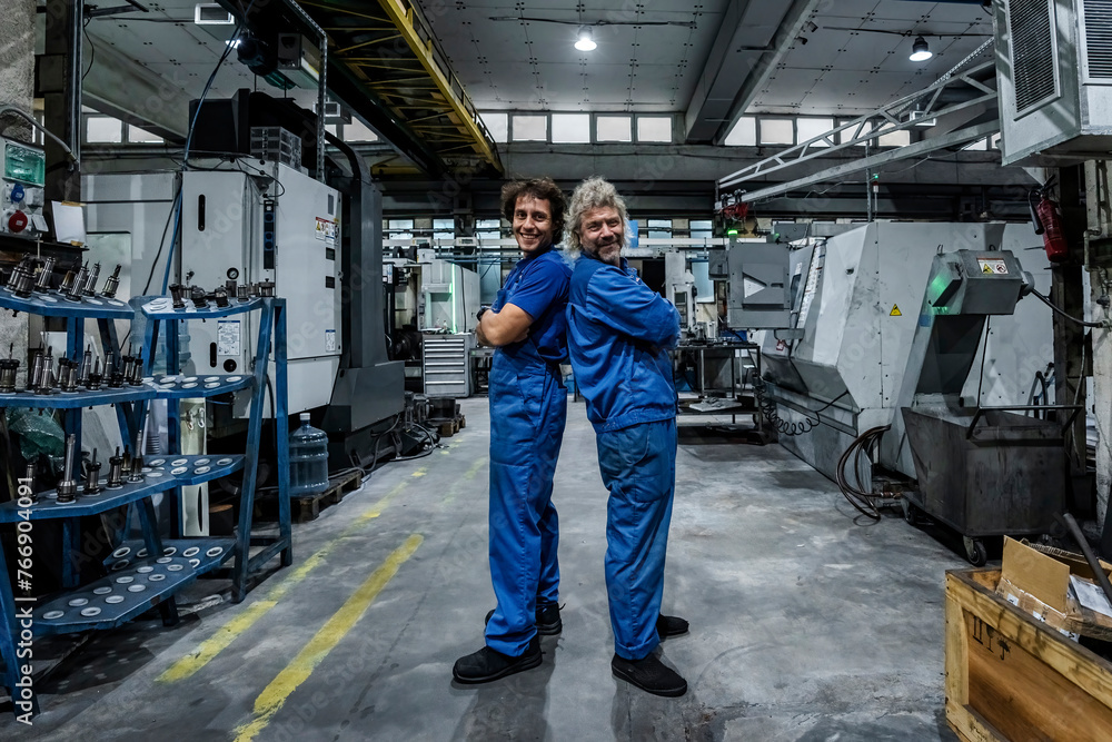 Smiling technicians standing back to back with arms crossed in industry Smiling technicians standing back to back with arms crossed in industry