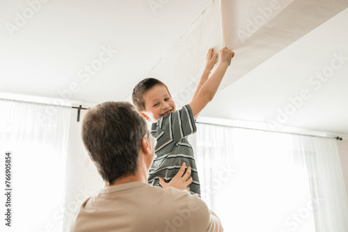Happy boy helping father in peeling old wallpaper from wall at home photo