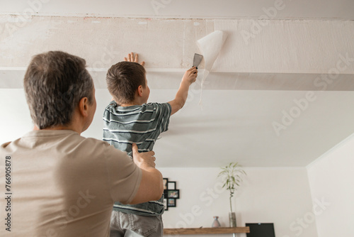Son and father peeling old wallpaper with spatula from wall at home photo